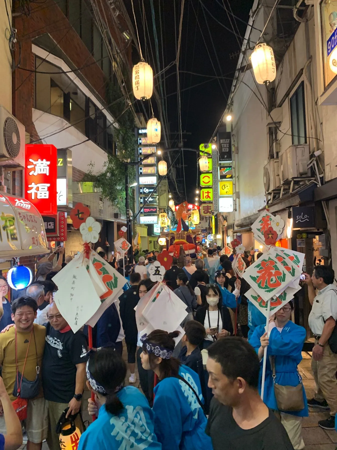 夜の繁華街を行く踊町の人たちと見物の人